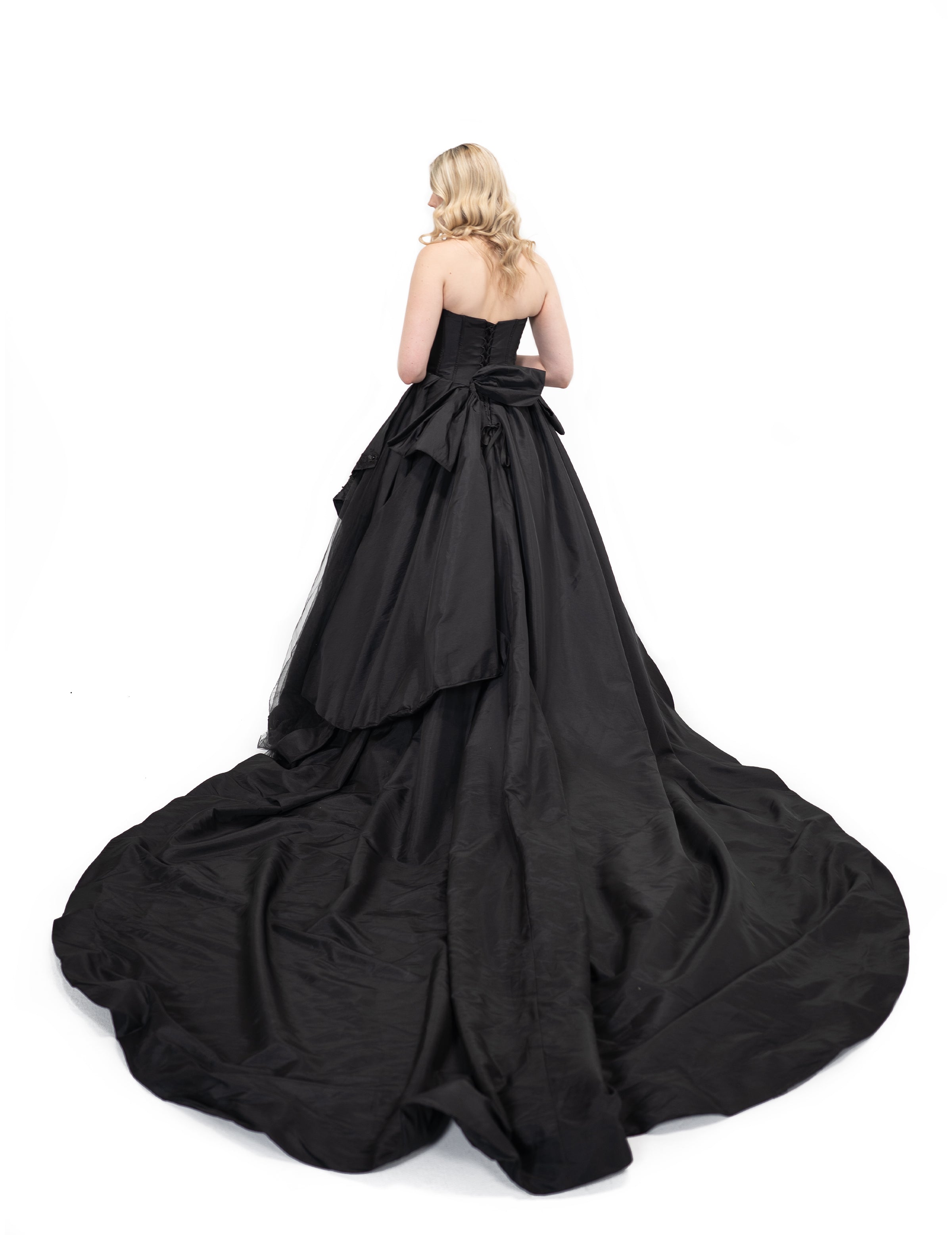 Black alternative wedding gown with extended flowing train and layered skirt, back angled view by Bête Noire