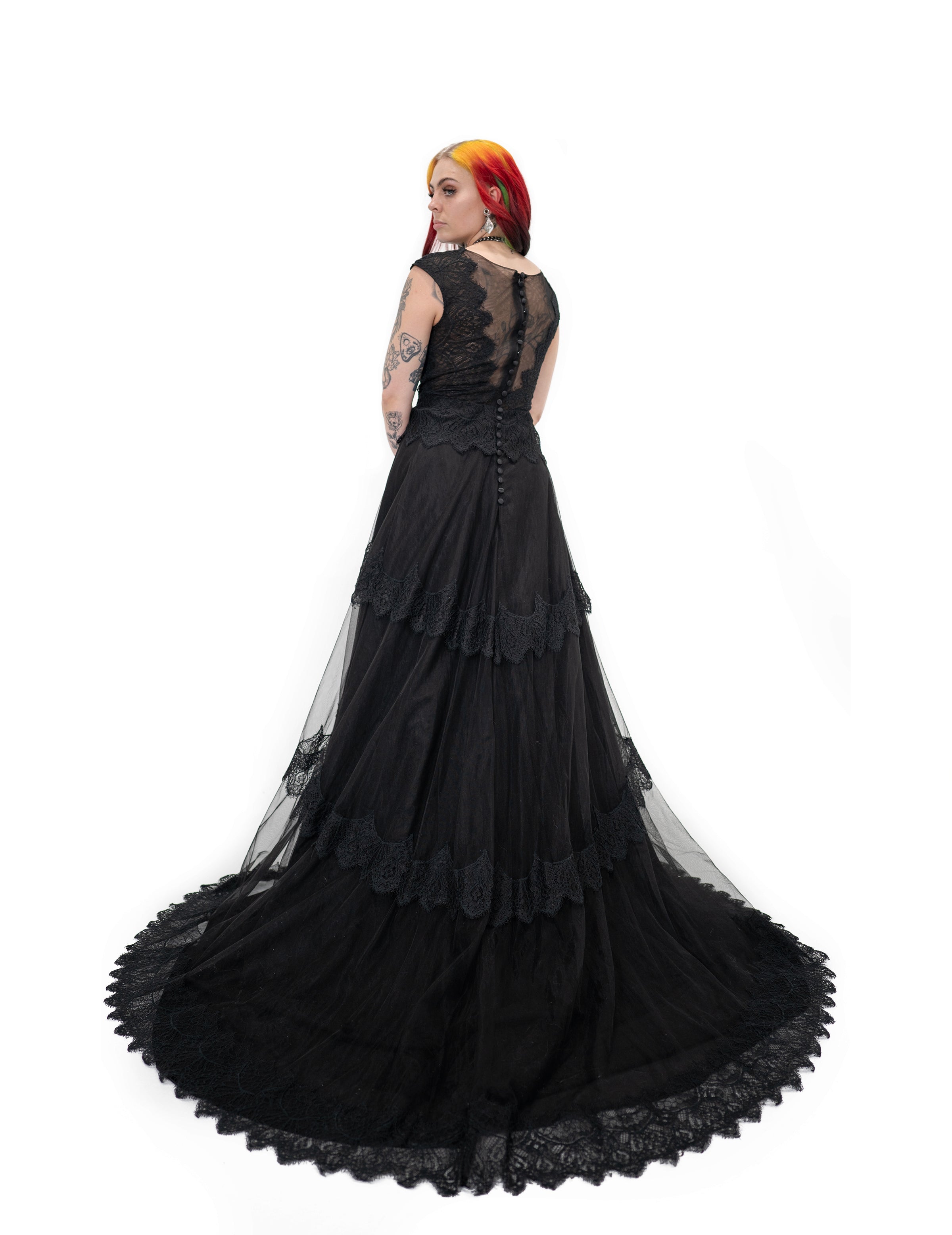 Side back view of Bête Noire Devotion gown showing layered skirt, lace trim, and long black train