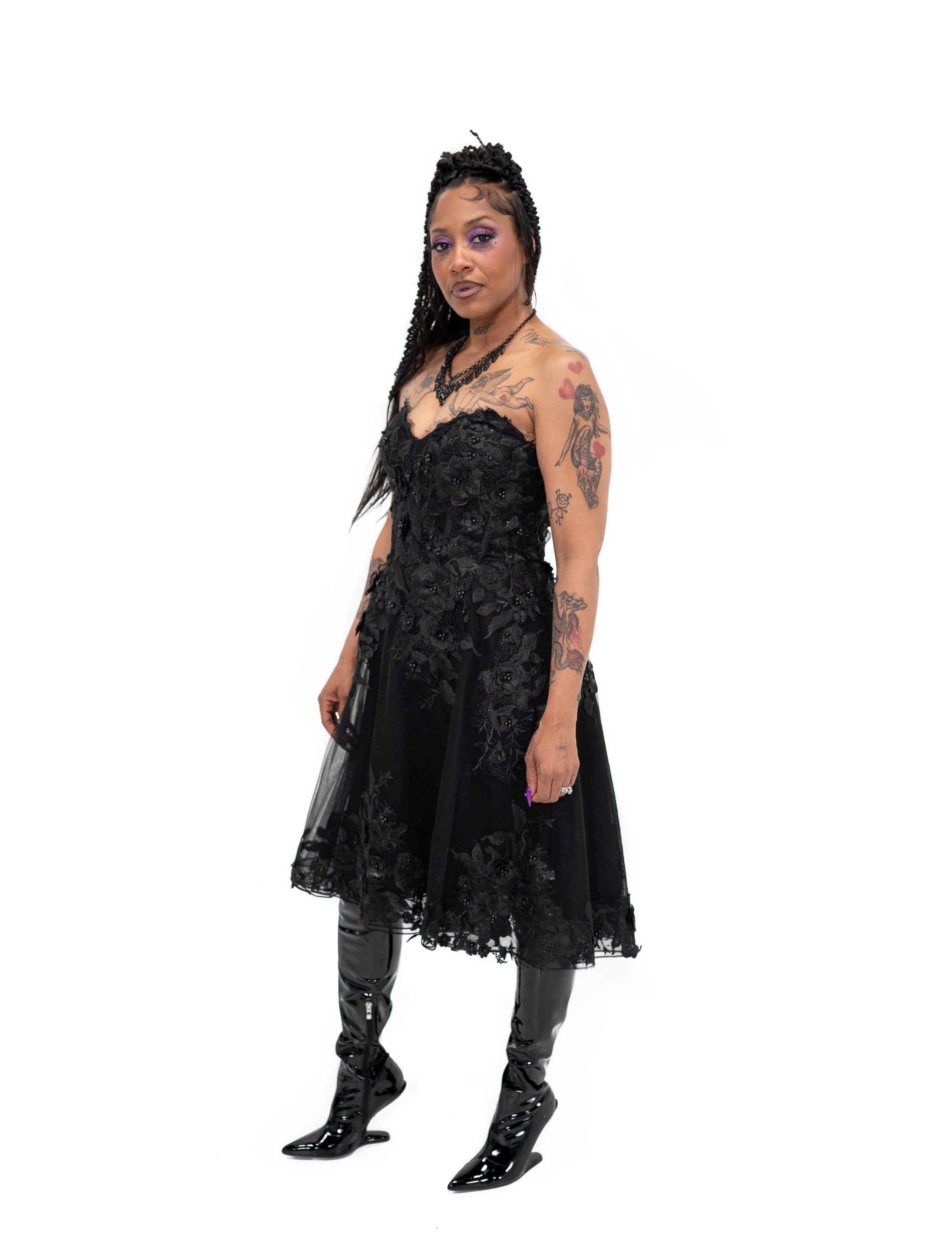 Angled view of Bête Noire Nyx dress, a black alternative bridal midi dress with floral lace and fitted corset bodice